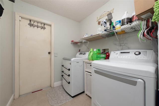 clothes washing area featuring a textured ceiling, separate washer and dryer, and light tile patterned floors