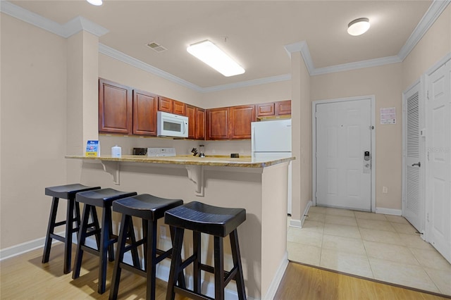 kitchen with white appliances, kitchen peninsula, a breakfast bar area, light hardwood / wood-style flooring, and ornamental molding