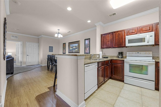 kitchen with light hardwood / wood-style floors, light stone counters, white appliances, kitchen peninsula, and a kitchen bar