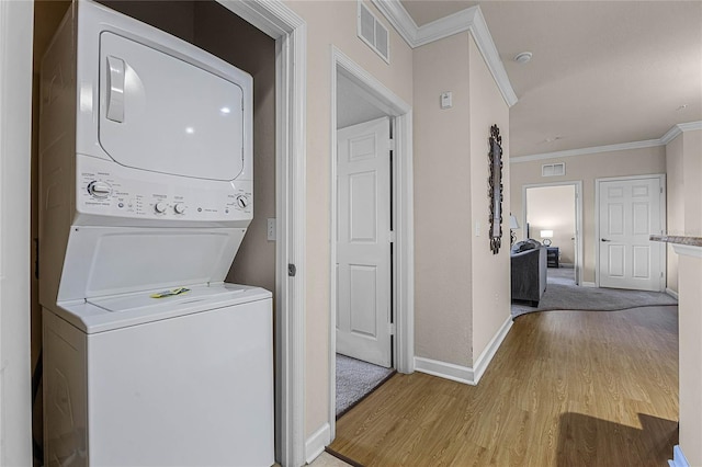 washroom featuring ornamental molding, stacked washer and dryer, and light hardwood / wood-style flooring