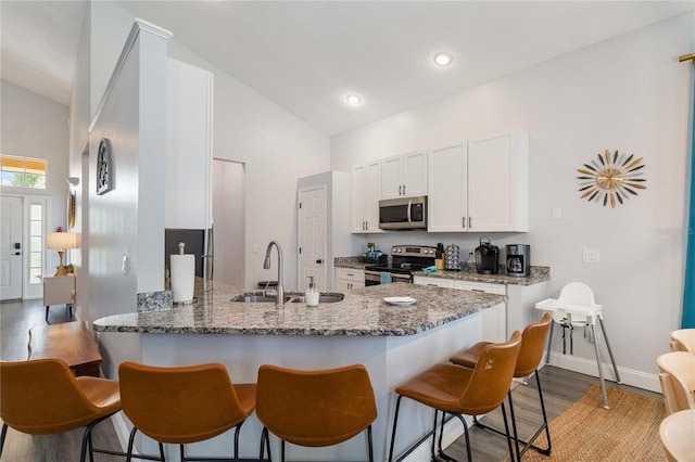 kitchen featuring appliances with stainless steel finishes, white cabinetry, kitchen peninsula, light stone countertops, and sink