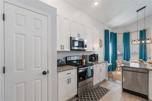 kitchen with dark stone counters, white cabinets, appliances with stainless steel finishes, and decorative light fixtures