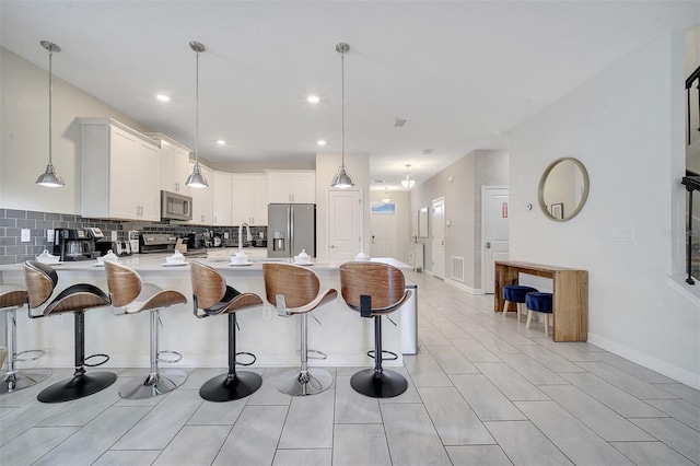 kitchen featuring decorative backsplash, a kitchen breakfast bar, stainless steel appliances, hanging light fixtures, and white cabinetry