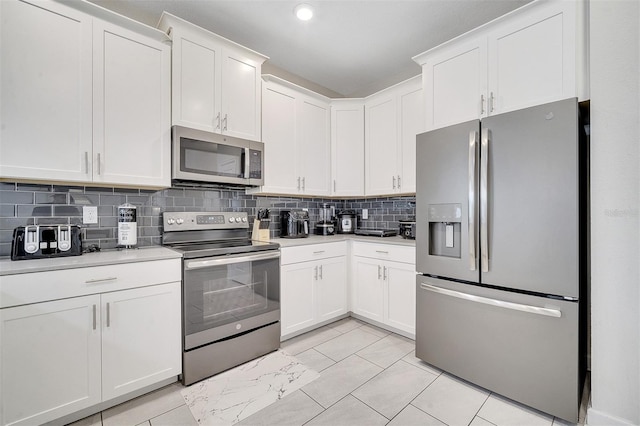 kitchen with appliances with stainless steel finishes, white cabinetry, light tile patterned floors, and tasteful backsplash