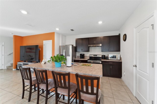 kitchen with dark brown cabinetry, a kitchen island with sink, stainless steel appliances, and a breakfast bar