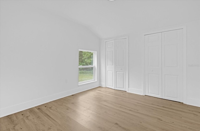 unfurnished bedroom featuring light hardwood / wood-style floors, vaulted ceiling, and two closets