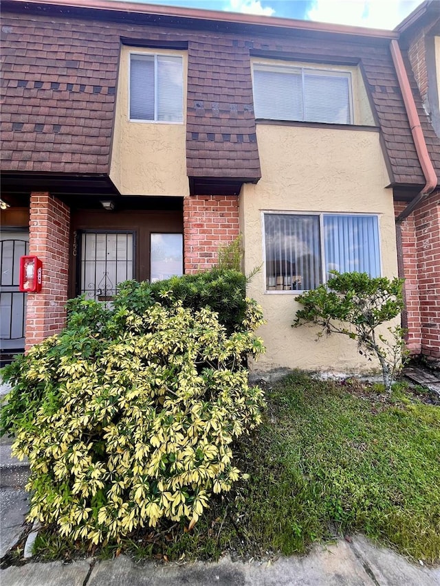 townhome / multi-family property with brick siding, mansard roof, and stucco siding