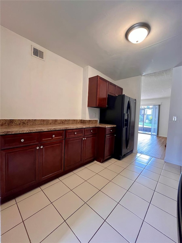 kitchen with black refrigerator with ice dispenser and light tile patterned flooring