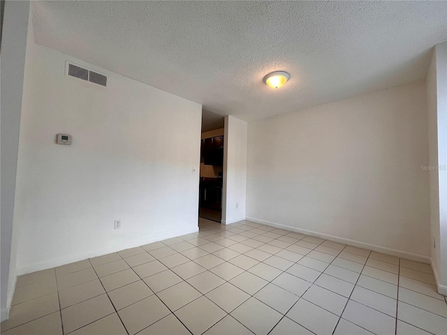 spare room featuring a textured ceiling, light tile patterned flooring, baseboards, and visible vents