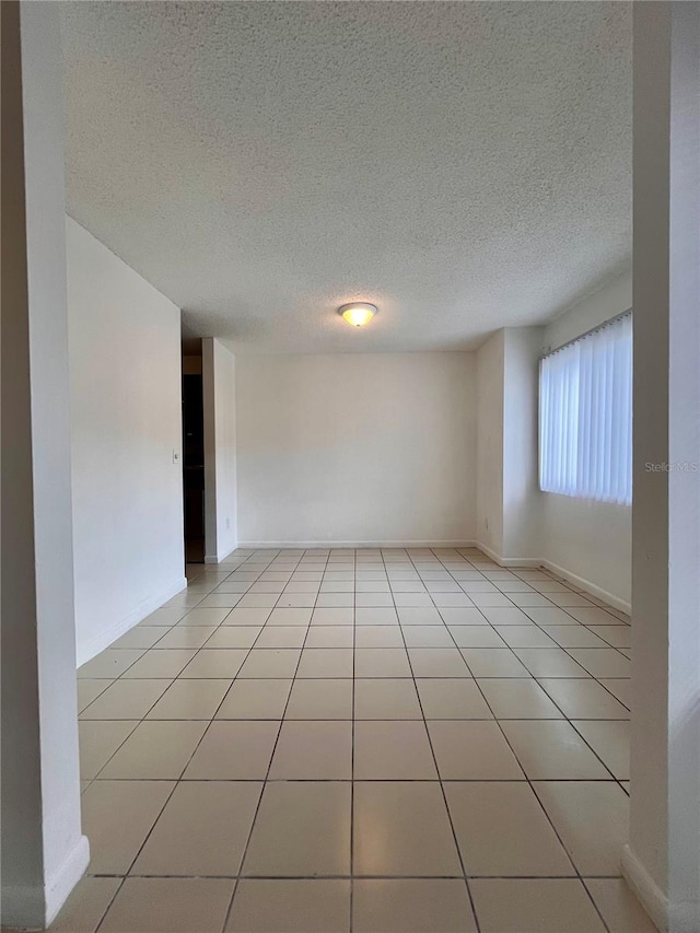 spare room with a textured ceiling, light tile patterned flooring, and baseboards