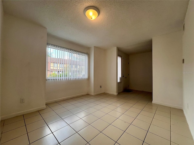 empty room with a textured ceiling, light tile patterned floors, and baseboards