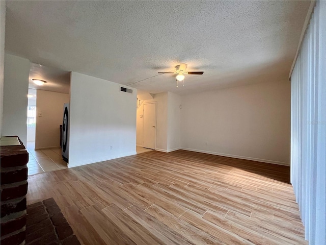 spare room with baseboards, light wood-type flooring, a textured ceiling, a ceiling fan, and visible vents