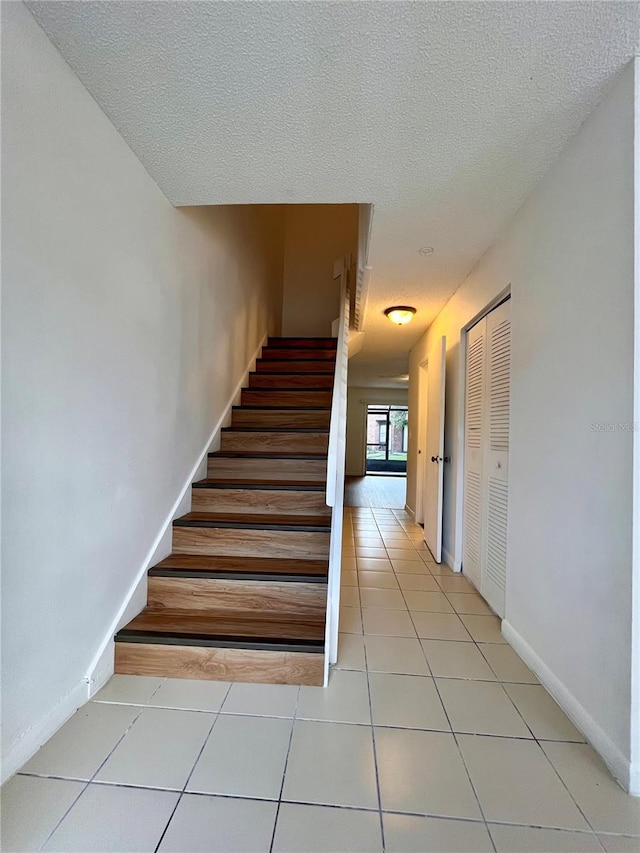 stairs with a textured ceiling, baseboards, and tile patterned flooring