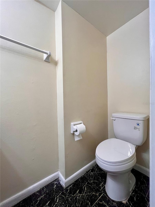 bathroom with toilet, marble finish floor, and baseboards