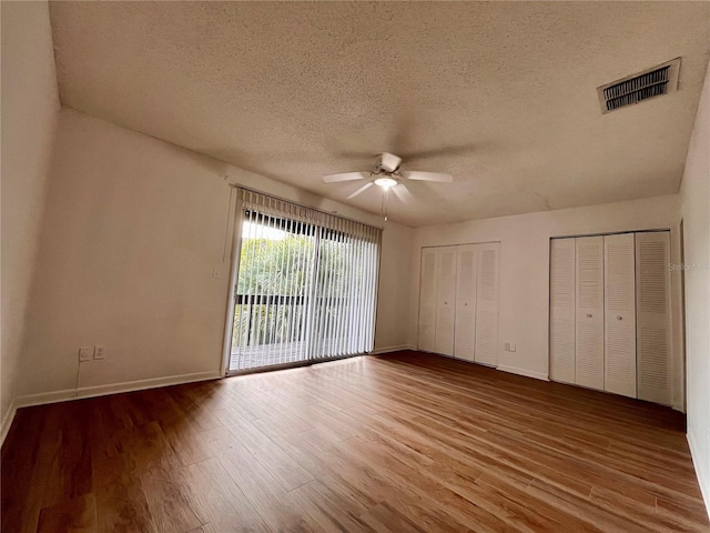 unfurnished bedroom with wood-type flooring, a textured ceiling, access to exterior, multiple closets, and ceiling fan