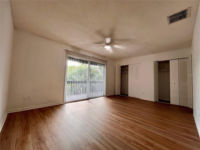 unfurnished bedroom with a textured ceiling, hardwood / wood-style flooring, access to exterior, multiple closets, and ceiling fan