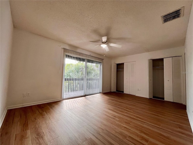 unfurnished bedroom with multiple closets, visible vents, access to exterior, and wood finished floors