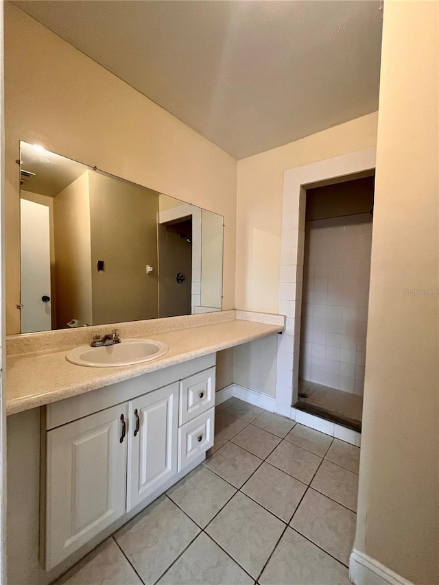 full bathroom with tile patterned flooring, vanity, baseboards, and a tile shower