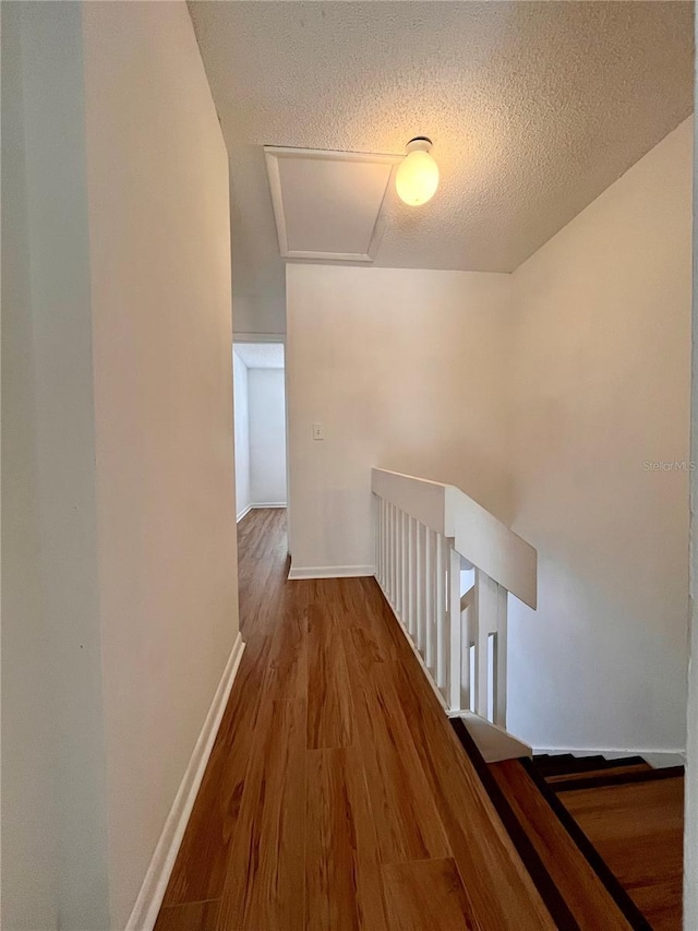 hall featuring baseboards, an upstairs landing, wood finished floors, and a textured ceiling