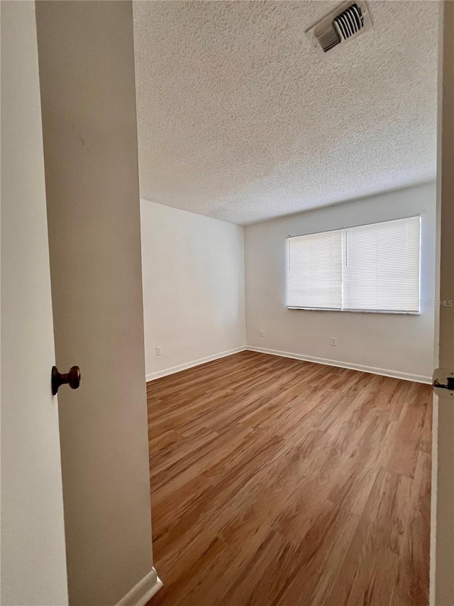 spare room with visible vents, baseboards, a textured ceiling, and wood finished floors