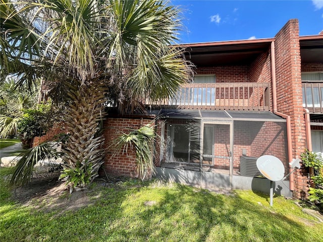 rear view of house with brick siding, cooling unit, a lawn, and a balcony