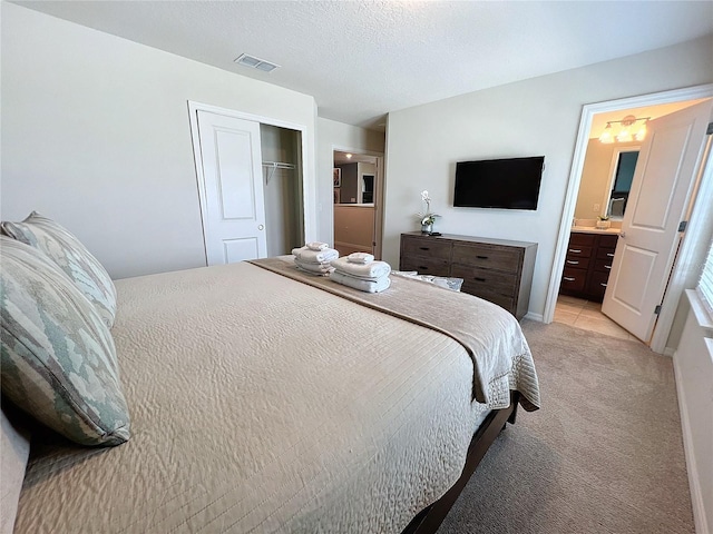 bedroom featuring a closet, connected bathroom, light carpet, and a textured ceiling