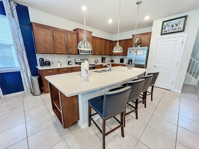 kitchen featuring sink, a kitchen bar, stainless steel appliances, pendant lighting, and a center island with sink