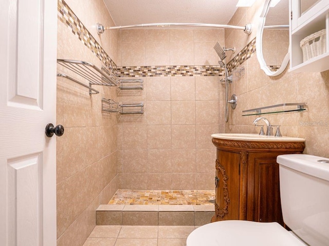 bathroom featuring tile patterned flooring, tiled shower, vanity, and toilet