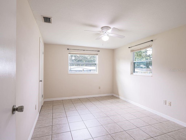 empty room featuring ceiling fan, light tile patterned floors, and a wealth of natural light