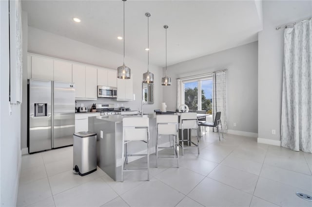 kitchen with appliances with stainless steel finishes, white cabinetry, pendant lighting, a kitchen bar, and a center island with sink