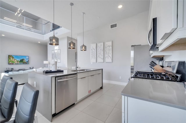 kitchen with light tile patterned flooring, white cabinets, stainless steel appliances, decorative light fixtures, and a center island with sink