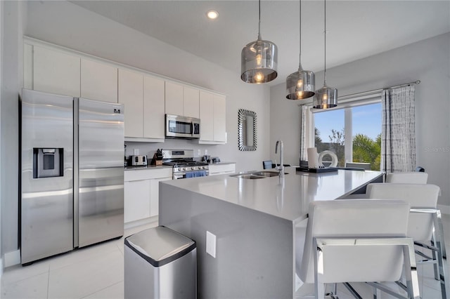 kitchen featuring a kitchen island with sink, sink, white cabinetry, stainless steel appliances, and decorative light fixtures