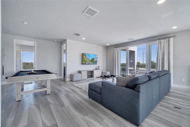 living room featuring pool table, a healthy amount of sunlight, a textured ceiling, and light wood-type flooring