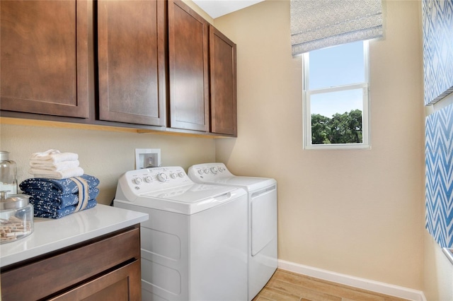 laundry room with light wood-type flooring, separate washer and dryer, and cabinets