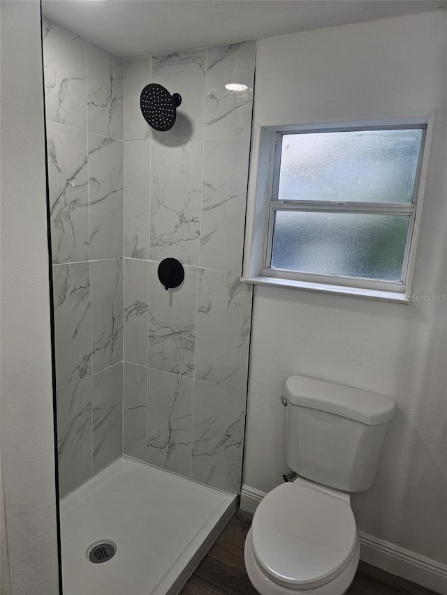 bathroom with toilet, a tile shower, and hardwood / wood-style flooring