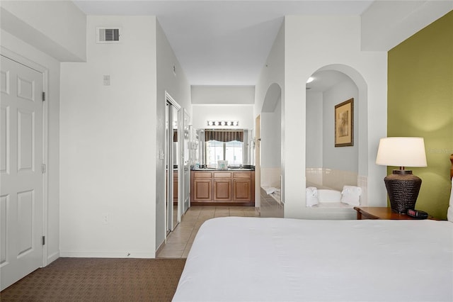 bedroom with ensuite bathroom and light tile patterned floors