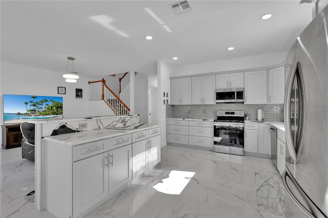 kitchen with light stone counters, white cabinets, decorative light fixtures, and stainless steel appliances