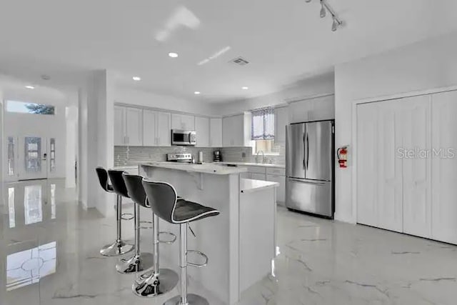 kitchen with a breakfast bar area, sink, a center island, white cabinets, and appliances with stainless steel finishes