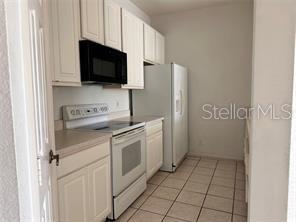 kitchen with light tile patterned floors, electric range, and white cabinetry