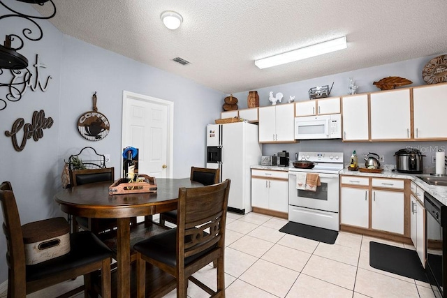 kitchen with white appliances, light tile patterned floors, visible vents, light countertops, and white cabinets