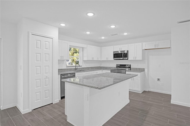 kitchen featuring light stone countertops, a center island, stainless steel appliances, and white cabinetry