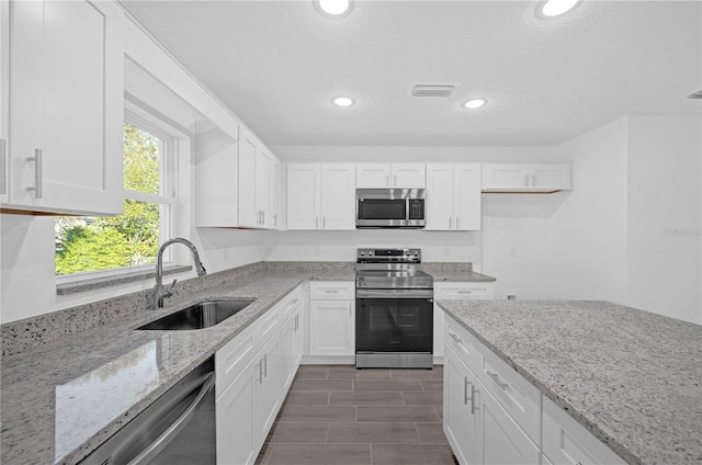 kitchen with white cabinetry, sink, light stone countertops, and appliances with stainless steel finishes