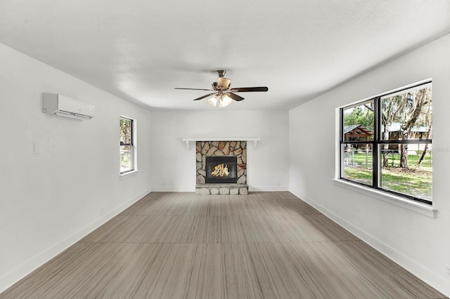 unfurnished living room with ceiling fan, a stone fireplace, a textured ceiling, and a wall unit AC