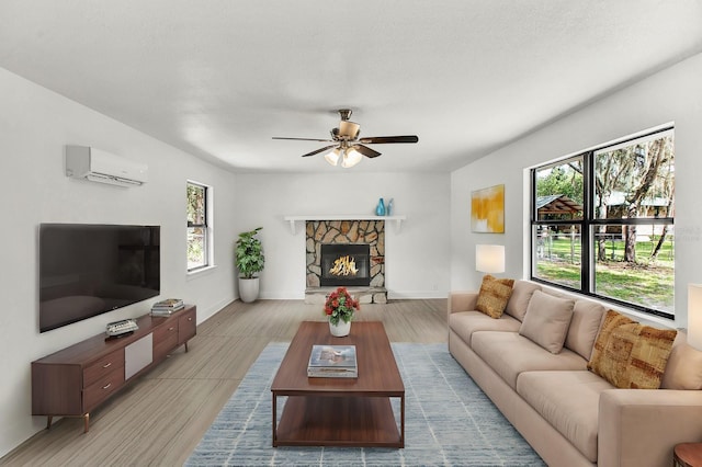 living room featuring a textured ceiling, a stone fireplace, ceiling fan, and a wall unit AC