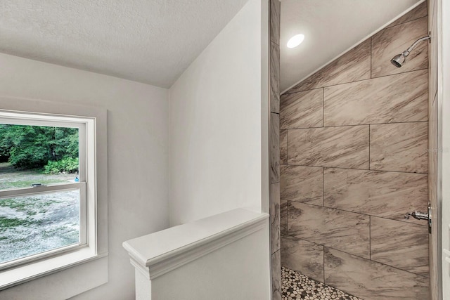 bathroom with vaulted ceiling, a textured ceiling, plenty of natural light, and tiled shower