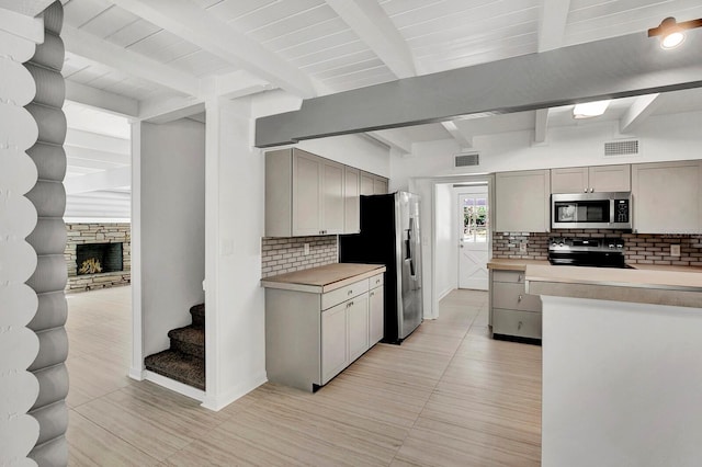 kitchen with beamed ceiling, tasteful backsplash, a fireplace, gray cabinetry, and appliances with stainless steel finishes