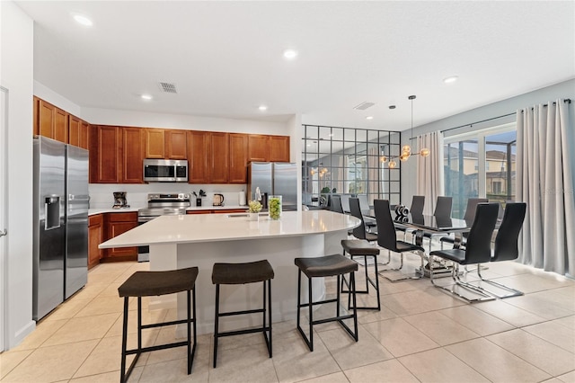 kitchen with decorative light fixtures, stainless steel appliances, a kitchen island with sink, a breakfast bar, and light tile patterned floors