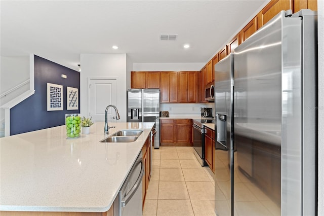 kitchen with light tile patterned floors, sink, stainless steel appliances, light stone counters, and a center island with sink