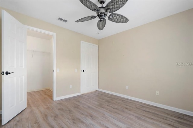 unfurnished bedroom with a closet, light hardwood / wood-style floors, ceiling fan, and a walk in closet