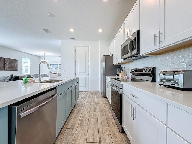 kitchen with light hardwood / wood-style floors, sink, white cabinets, backsplash, and appliances with stainless steel finishes